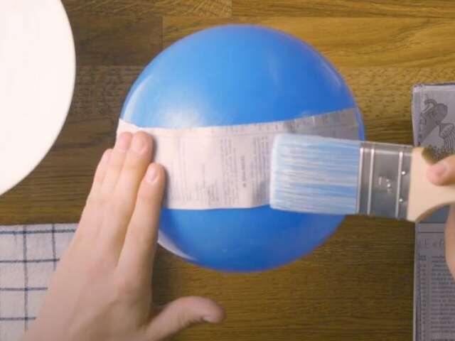 Sticking newspaper to a balloon using glue during a paper mache craft.