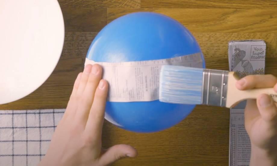 Sticking newspaper to a balloon using glue during a paper mache craft.