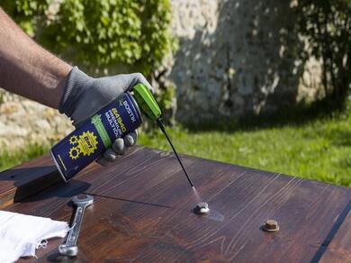 Bostik BA940 Premium Multi‑Use Spray applied to rusted bolts on a wooden surface during an outdoor DIY task.