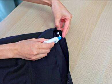 Bostik Fabric Glue being applied to the hem of a black garment to bond fabric edges and repair clothing without stitching.