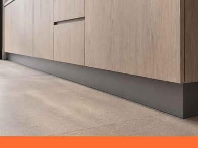 Moderne keuken met licht houten kastdeuren en een strak gemonteerde grijze plint voor een nette en afgewerkte uitstraling.