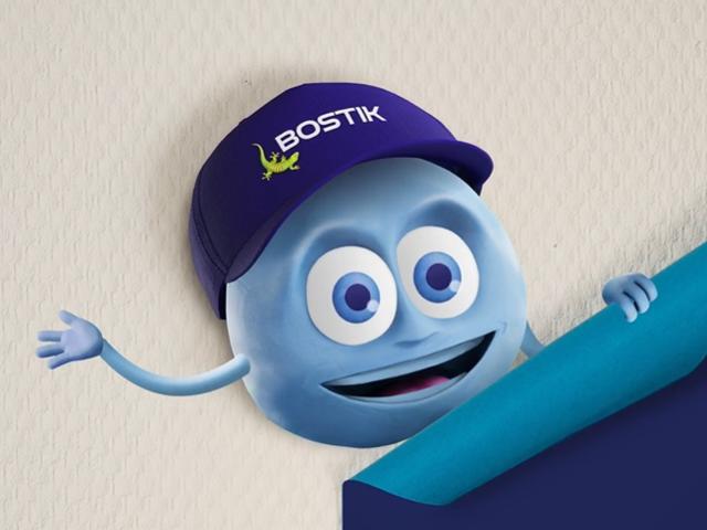 Blue Bostik gecko mascot wearing a purple Bostik cap peeks over a rolled sheet of blue material against a light textured background. The cartoon character features large eyes and outstretched arms, with the Bostik logo visible on the cap.