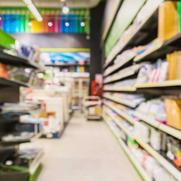 Ryškiai apšviesta parduotuvės praėjimo zona su lentynomis, pilnomis statybinių ir remonto prekių, tinkamų Bostik produktų įsigijimui.